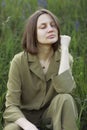 Portrait of a young woman sitting in a field on the spring grass among purple flowers. stylish girl enjoys Sunny spring weather. Royalty Free Stock Photo