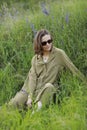 Portrait of a young woman sitting in a field on the spring grass among purple flowers. stylish girl wearing sunglasses Royalty Free Stock Photo