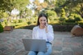 Portrait of a young woman sitting at a laptop in the park. Talk on mobile phone