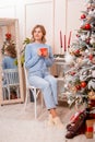 Portrait of a young woman sitting with a mug in her hands next to a Christmas tree