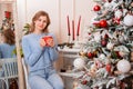 Portrait of a young woman sitting with a mug in her hands next to a Christmas tree