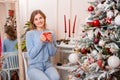 Portrait of a young woman sitting with a mug in her hands next to a Christmas tree