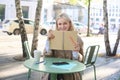 Portrait of young woman sitting in outdoor cafe, hiding behind journal, holding notebook in hands and smiling Royalty Free Stock Photo