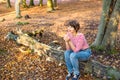 Portrait of young woman sitting and relaxing on the fallen tree in autumnal forest. looking away. smiling girl. Autumn outdoor Royalty Free Stock Photo