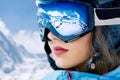 Portrait of young woman at the ski resort on the background of mountains and blue sky.A mountain range reflected in the ski mask. Royalty Free Stock Photo