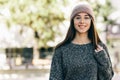 Portrait of young woman smiling, wearing transparent eyeglasses, gray sweater and pink hat. Outdoor image of pretty student girl Royalty Free Stock Photo