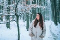 Portrait of a young woman in snow trying to warm herself. Beautiful girl in the winter forest in white down jacket. Royalty Free Stock Photo