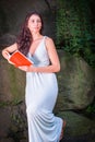 Portrait of Young Woman standing outdoors by rocks in hot summer, reading red book Royalty Free Stock Photo