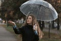 Portrait of young woman standing under transparent umbrella to see if it is raining. Girl with brown hair walks in park Royalty Free Stock Photo