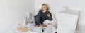 Portrait of young woman, student studying in her bed, relaxing while preparing homework, eating doughnut, using laptop Royalty Free Stock Photo