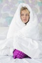 Portrait of young woman suffering from fever while wrapped in quilt in bed