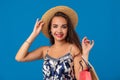 Portrait of a young woman in summer hat holding shopping bags and looking at the camera isolated over blue background Royalty Free Stock Photo