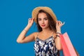 Portrait of a young woman in summer hat holding shopping bags and looking at the camera isolated over blue background Royalty Free Stock Photo