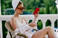 Portrait of young woman in sunglasses sits on the balcony and uses the phone Perfect sunny morning Royalty Free Stock Photo