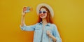 Portrait of young woman taking selfie picture by phone wearing a straw hat in the city over orange background Royalty Free Stock Photo