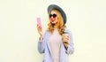 Portrait young woman using phone holding coffee cup, curly hair, wearing round hat, coat jacket on background Royalty Free Stock Photo