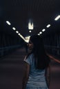 Portrait of young woman walks alone in a dark tunnel. Girl look back in low lighted underpass Royalty Free Stock Photo