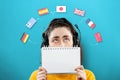 Portrait of a young woman wearing headphones, holding a notebook and looking up at the flags of different countries Royalty Free Stock Photo