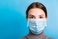 Portrait of young woman wearing medical mask with epidemic word at blue background. Protect your health. concept