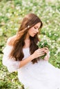 Portrait of a young woman in a white dress with primroses. A girl in the spring forest. White anemones in long brown hair