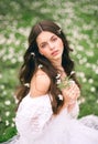 Portrait of a young woman in a white dress with primroses. A girl in the spring forest. White anemones in long brown hair