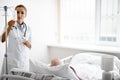 Young doctor adjusting infusion bottle while standing near patient bed Royalty Free Stock Photo