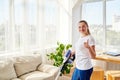 Portrait of young woman in white shirt and jeans cleaning carpet with vacuum cleaner in living room and showing thumb up gesture. Royalty Free Stock Photo