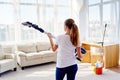 Portrait of young woman in white shirt and jeans holding in hands wireless vacuum cleaner while cleaning in living room at home. Royalty Free Stock Photo