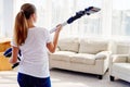 Portrait of young woman in white shirt and jeans holding in hands wireless vacuum cleaner while cleaning in living room at home. Royalty Free Stock Photo