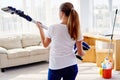 Portrait of young woman in white shirt and jeans holding in hands wireless vacuum cleaner while cleaning in living room at home. Royalty Free Stock Photo