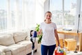 Portrait of young woman in white shirt and jeans holding in hands wireless vacuum cleaner and detergents while cleaning at home Royalty Free Stock Photo