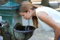 Portrait of young woman who hydrates herself drinking water from a fountain during heat wave on summer