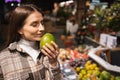 Portrait of a young woman who sniffing fresh mango in a supermarket. Girl buys fruit at the grocery store.