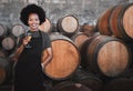 Portrait of a young woman winemaker standing with a glass with wooden barrel of red wine in a winery cellar or