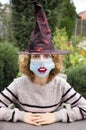 Portrait of a young woman in a witch hat and a medical mask with painted lips on it, funny rounded eyes Royalty Free Stock Photo