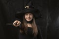 Portrait of young woman in witches pointed hat with magic wand in her hands on black background. Young witch