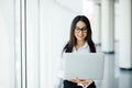 Portrait of young business woman working holding laptop standing against panoramic window with city view Royalty Free Stock Photo