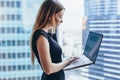 Portrait of young woman working holding laptop standing against panoramic window with city view Royalty Free Stock Photo