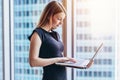 Portrait of young woman working holding laptop standing against panoramic window with city view Royalty Free Stock Photo