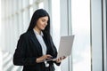 Portrait of young woman working holding laptop standing against panoramic window with city view Royalty Free Stock Photo