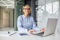 Portrait of a young woman working in the office using a laptop, looking and smiling at the camera while sitting at a Royalty Free Stock Photo