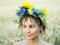 Portrait of a young woman in a wreath of wild flowers stands in the field at sunset.