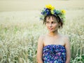 Portrait of a young woman in a wreath of wild flowers stands in the field at sunset.