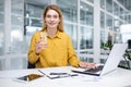 Portrait of a young woman in a yellow shirt working in the office at a laptop and drinking water from a glass, smiling Royalty Free Stock Photo