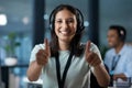Well done is what were aiming for. Portrait of a young woman using a headset and showing thumbs up in a modern office. Royalty Free Stock Photo