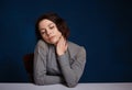 Young worried woman. She sits at a table against on a dark blue background Royalty Free Stock Photo