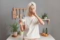 Portrait of young yawning woman in towel wrapped around hair, with morning cup of coffee, standing in kitchen, sleepy tired girl Royalty Free Stock Photo