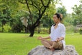 Portrait of young yogi man in white shirt doing yoga meditation while sitting in lotus position on the rock in beautiful outdoor p Royalty Free Stock Photo