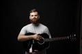 Portraite of bearded man musician, guitarist standing and holding a acoustic guitar in a hand and looks in a camera.