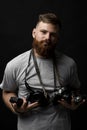 Portraite of bearded professional photographer in a grey t-shirt with a bunch of different cameras in a hands and on a
